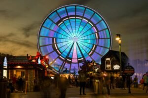 A vibrant ferris wheel lights up the night sky at a bustling theme park.
